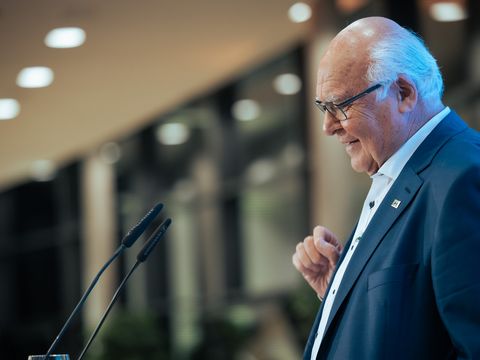 älterer grauhaariger Mann steht an einem Mikrofon