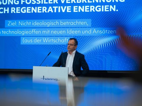älterer Mann mit Brille und Anzug auf einer Bühne am Mikrofon und hält ein Vortrag