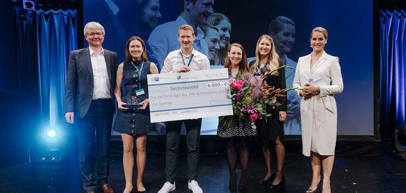 Geschäftsleitung Miriam Häring steht mit fünf weitere Personen auf der Bühne und hält den Bildungspreis 2022 in der Hand