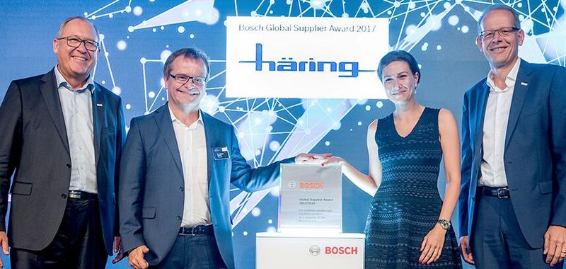 Geschäftsleitung Jürgen und Miriam Häring stehen mit zwei männliche Personen auf der Bühne mit einer Auszeichnung für "Bosch Global Supplier Award 2017"
